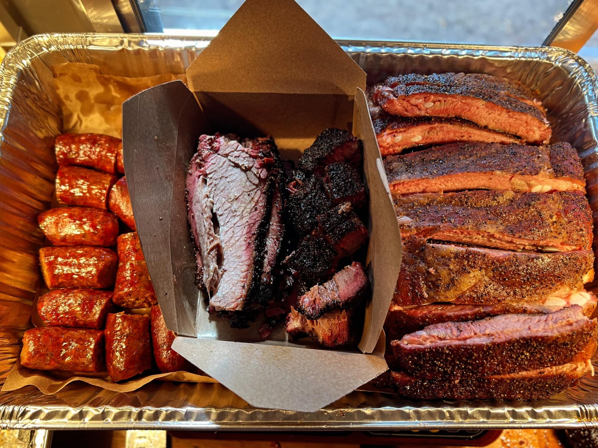 Professional meat platter with brisket, ribs, sausage, sides and pickles
