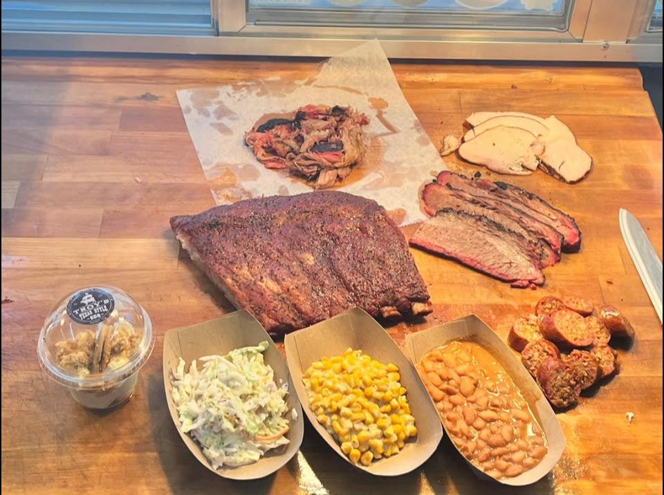 Brisket flat with ribs and pulled pork sides on wooden table, full platter display